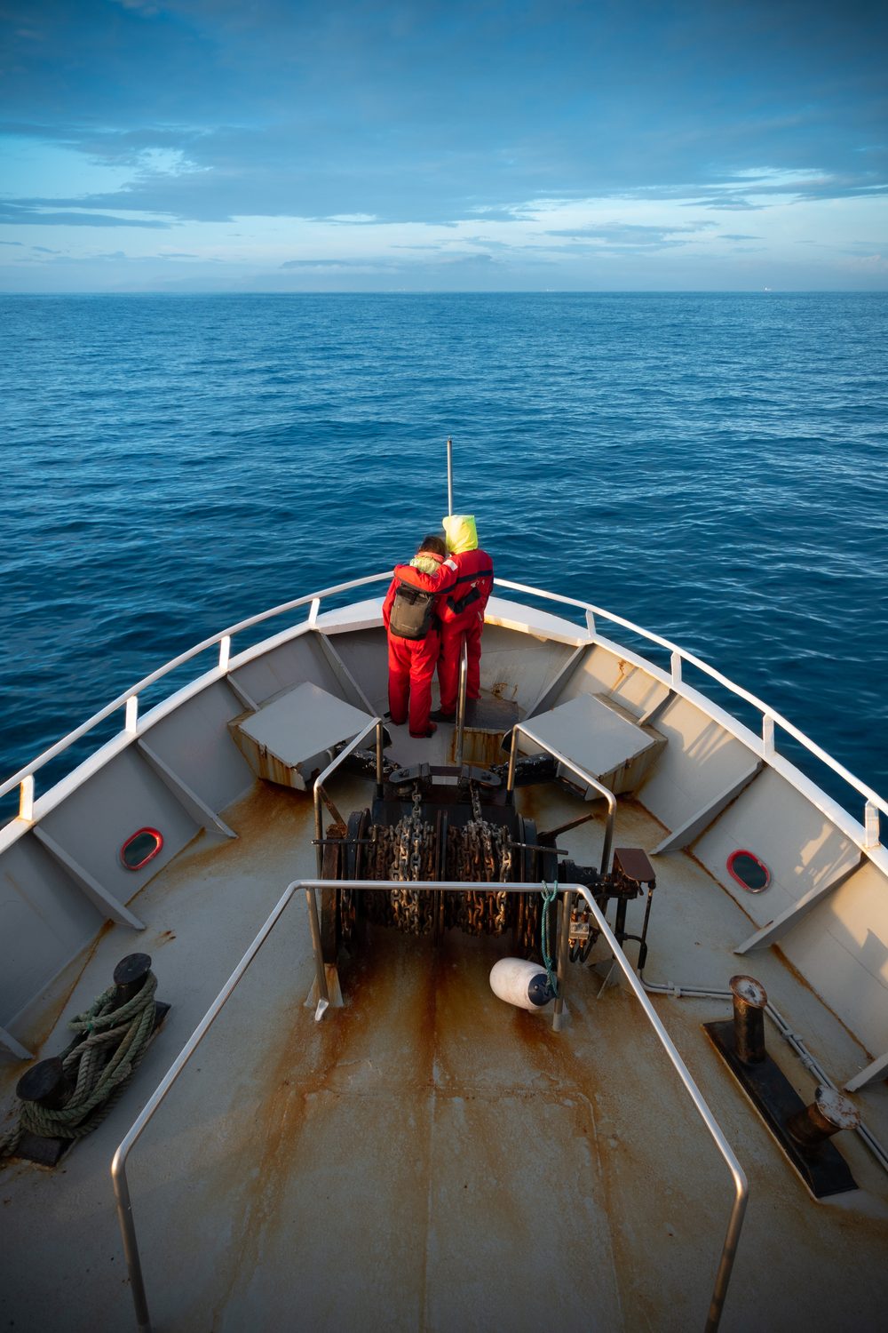 Two crew at the bow of a vessel in open water
