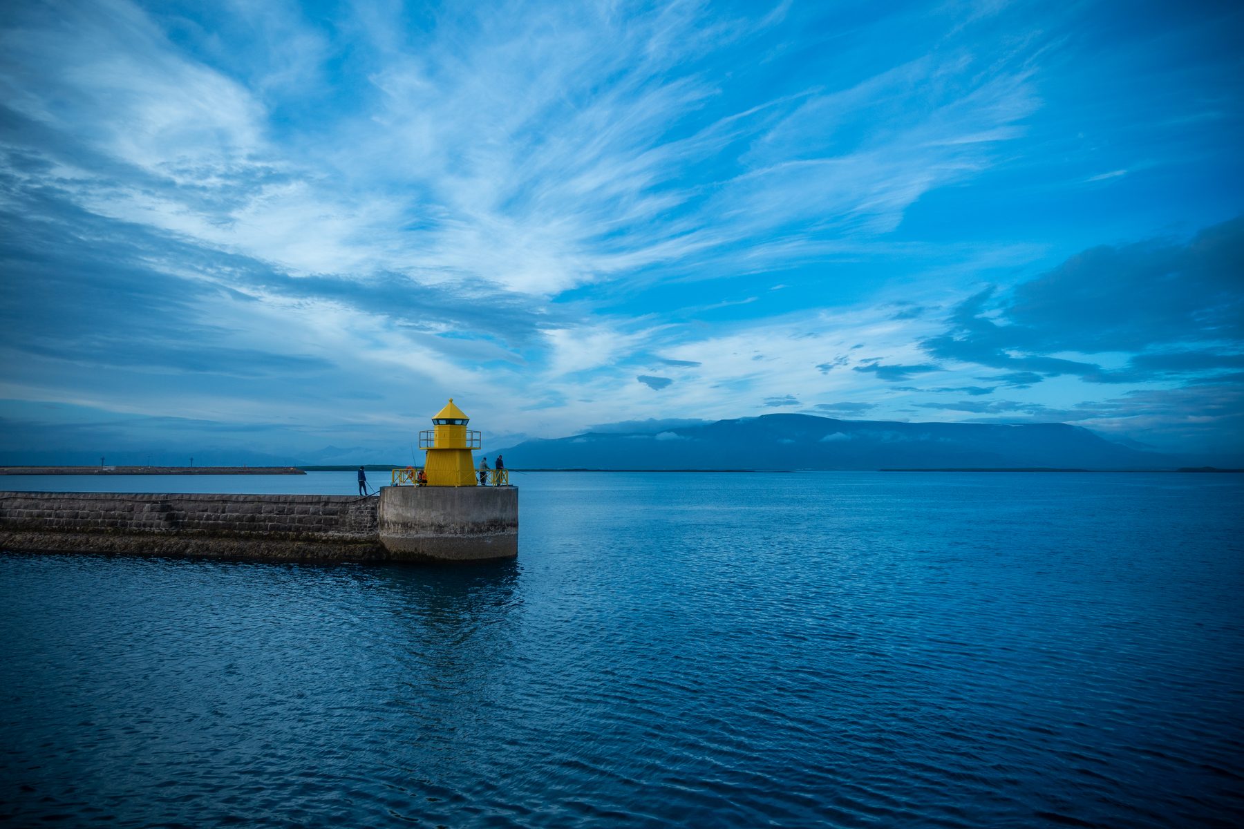 A small yellow lighthouse at the end of a harbour wall